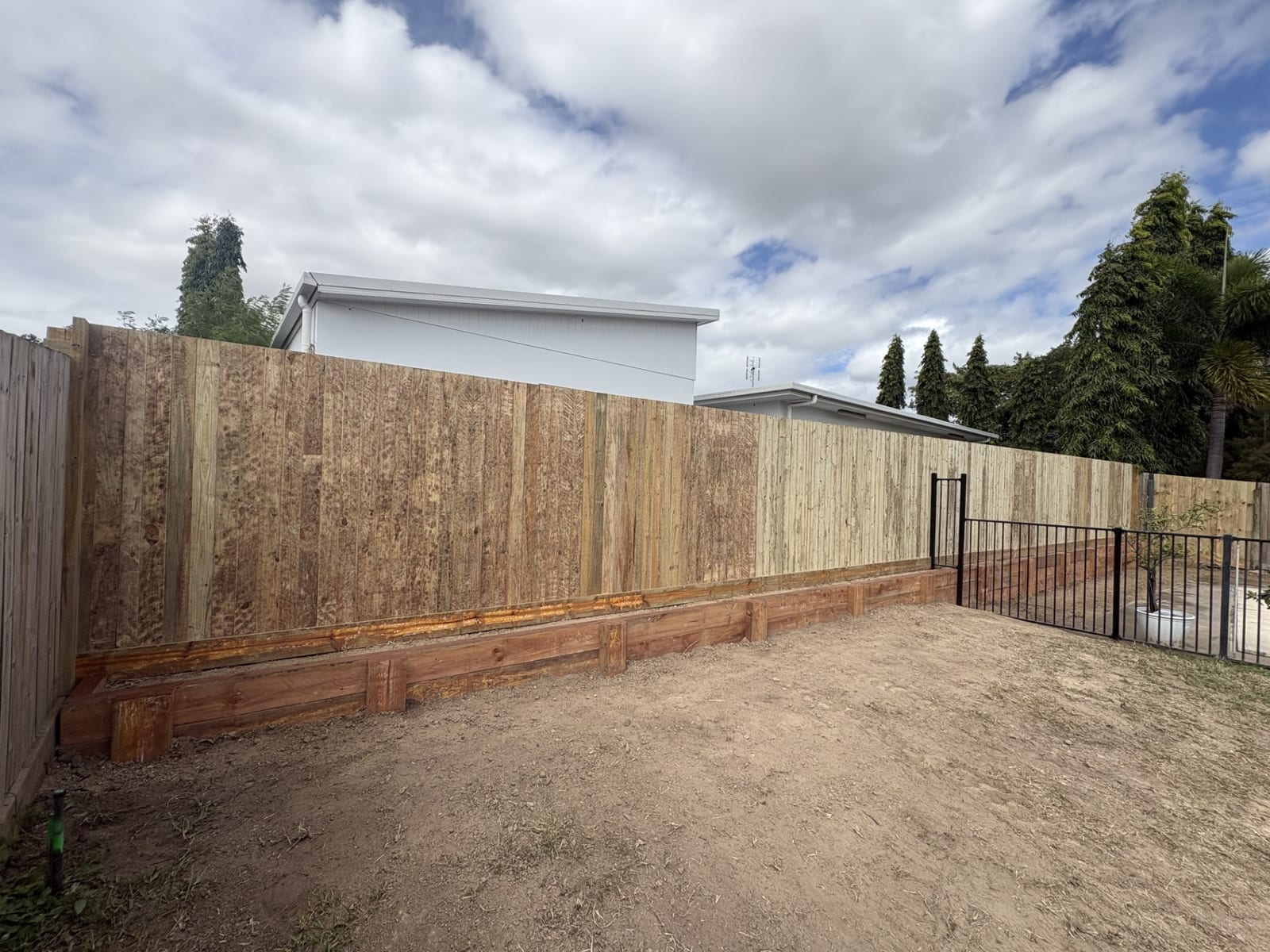 Sleeper retaining wall under a new timber fence, Townsville